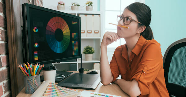 Woman holding pen under her nose in front of computer with visual elements