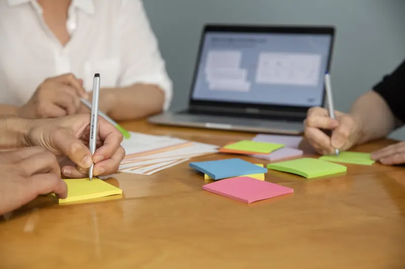 Hands writing on sticky notes around a laptop in a legal design workshop